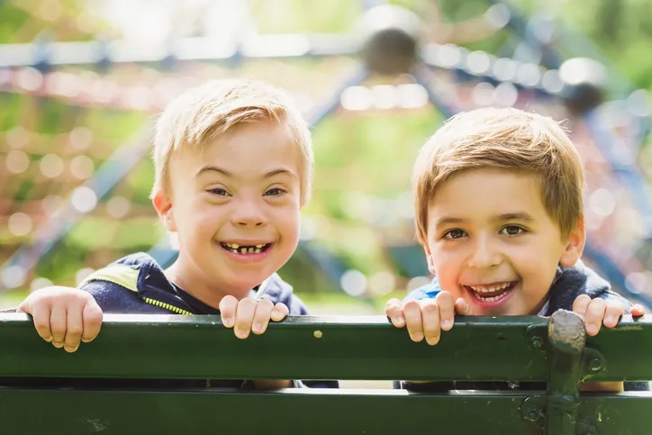 Zwei Jungen mit fröhlichen Gesichtern, die über eine Spielplatzbank schauen und lächeln.